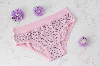 Beyaz yapılı arka planda çiçek tomurcukları olan pembe pamuklu külotlar. Kadın iç çamaşırı seti. Üst görünüm.