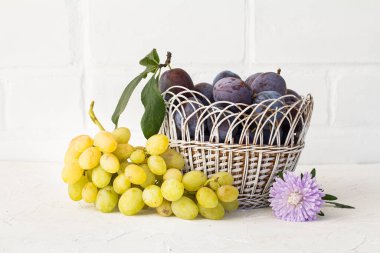 Hasır bir sepette olgun erikler ve beyaz arka planda kasımpatı çiçeği olan olgun beyaz üzümler topladım. Sadece meyve topladım..