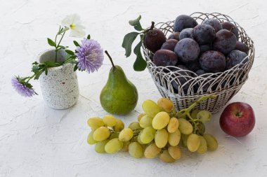 Hasır sepette olgun erikler, bir elma, bir armut ve beyaz yapılı arka planda bir demet olgun beyaz üzüm topladım. Sadece meyve topladım. Topv görünümü.