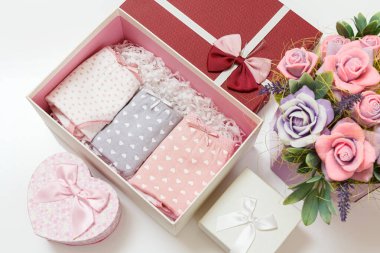 Beyaz arka planda suni çiçekler olan bir kutuda farklı renklerde katlanmış pamuk külotlar. Kadın iç çamaşırı seti. Üst görünüm.