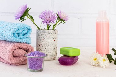 Deniz tuzu, bir şişe şampuan, terli havlular, sabun ve beyaz arka planda çiçekler. Banyo yapmak için kadın aksesuarları.