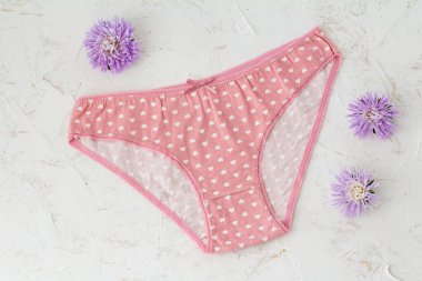 Beyaz yapılı arka planda çiçek tomurcukları olan pembe pamuklu külotlar. Kadın iç çamaşırı seti. Üst görünüm.