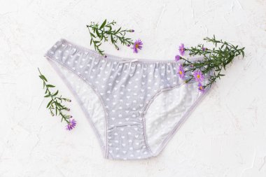 Beyaz yapılı arka planda çiçekli gri pamuklu külotlar. Kadın iç çamaşırı seti. Üst görünüm.