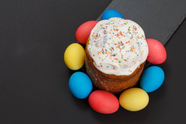 Tatlı Paskalya pastası ve siyah arkaplanlı renkli Paskalya yumurtaları. Üst görünüm.