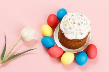 Renkli Paskalya yumurtaları ve pembe arka planda lale çiçekli bir tabakta paskalya pastası. Geleneksel Ortodoks Hıristiyan Paskalya yemeği. Üst görünüm.