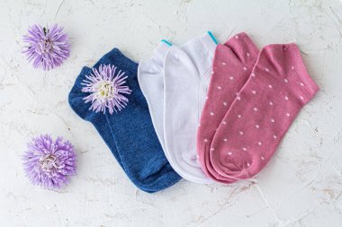 Beyaz yapılı arka planda beyaz çiçek tomurcukları olan üç çift mavi, beyaz ve pembe kadın çorabı..