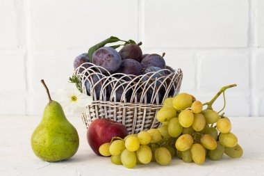 Hasır bir sepette olgun erikler, bir elma, bir armut ve beyaz arka planda bir demet olgun beyaz üzüm topladım. Sadece meyve topladım..
