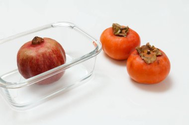 Cam bir kasede nar meyvesi ve beyaz arka planda olgun hurma meyveleri. Organik meyveler.