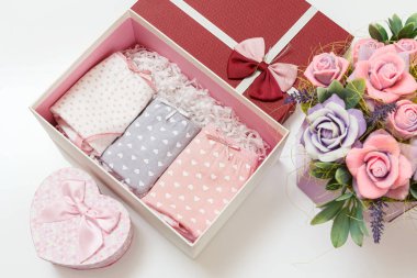 Beyaz arka planda suni çiçekler olan bir kutuda farklı renklerde katlanmış pamuk külotlar. Kadın iç çamaşırı seti. Üst görünüm.