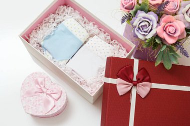 Beyaz arka planda suni çiçekler olan bir kutuda farklı renklerde katlanmış pamuk külotlar. Kadın iç çamaşırı seti. Üst görünüm.