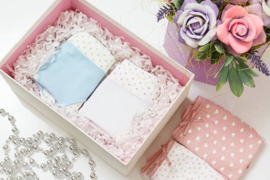 Beyaz arka planda suni çiçekler olan bir kutuda farklı renklerde katlanmış pamuk külotlar. Kadın iç çamaşırı seti. Üst görünüm.