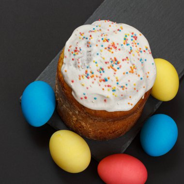 Tatlı Paskalya pastası ve siyah arkaplanlı renkli Paskalya yumurtaları. Üst görünüm.