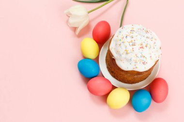 Lale çiçekli bir tabakta Paskalya pastası ve pembe arka planda renkli Paskalya yumurtaları. Geleneksel Ortodoks Hıristiyan Paskalya yemeği. Üst görünüm.