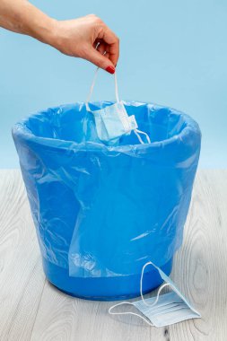 Tıbbi koruyucu maskeler kullanılmış. Bireysel korunma için kullanılacak çöp kutusu, salgın sırasında kullanılacak. Kadın eli ve mavi çöp torbası. Çevre kirliliği.