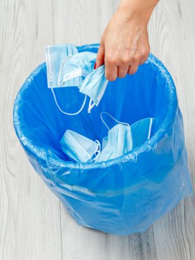 Tıbbi koruyucu maskeler kullanılmış. Bireysel korunma için kullanılacak çöp kutusu, salgın sırasında kullanılacak. Kadın eli ve mavi çöp torbası. Çevre kirliliği. Üst görünüm.