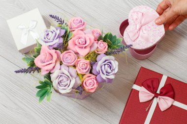 Gri ahşap arka planda gül şeklinde sabunlu, kalp şeklinde bir hediye kutusunu tutan kadının eli. Tatillerde hediye verme kavramı. Üst görünüm.