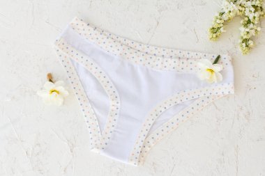 Beyaz yapılı arka planda nergis çiçeği tomurcukları olan beyaz pamuk külotlar. Kadın iç çamaşırı seti. Üst görünüm.