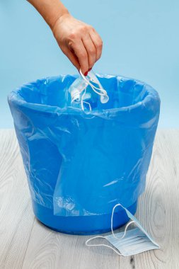 Tıbbi koruyucu maskeler kullanılmış. Bireysel korunma için kullanılacak çöp kutusu, salgın sırasında kullanılacak. Kadın eli ve mavi çöp torbası. Çevre kirliliği.
