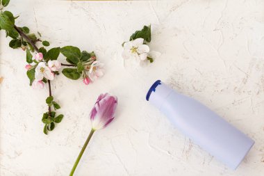 Yapılandırılmış arka planda bir şişe şampuan, lale ve elma ağacı çiçeği. Banyo prosedürleri için kadın aksesuarları. Üst görünüm.
