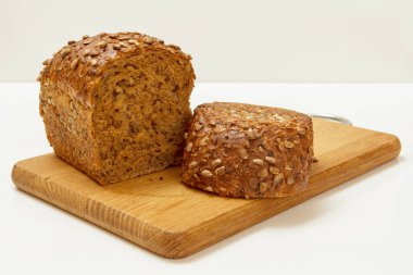 Beyaz arka planı olan tahta kesme tahtasının üzerinde çavdar ekmeği kes..