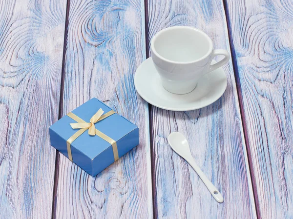 Фарфоровая чашка с блюдцем, ложкой и подарочной коробкой на деревянном фоне. — стоковое фото