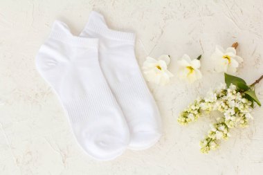 Pair of white socks, jasmine flowers and buds of daffodil flowers on the white structured background, Top view.