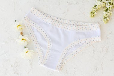 White cotton panties with jasmine flowers, buds of daffodil flowers on the white structured background. Woman underwear set. Top view.
