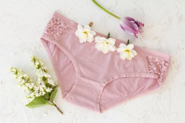 Pink cotton panties with buds of daffodil flowers, a tulip and a branch of jasmine with flowers on the white structured background. Woman underwear set. Top view.