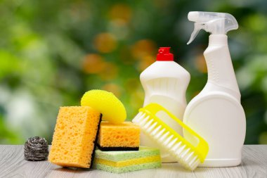 Bulaşık deterjanı, cam ve fayans temizleyicisi ve bulanık arka planda süngerler..