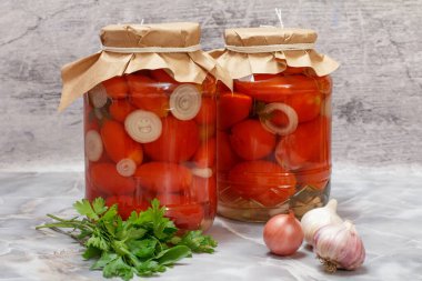 Cam kavanozlarda ve maydanoz yapraklarında saklanmış domatesler, sarımsak ve mutfak masasında soğan..