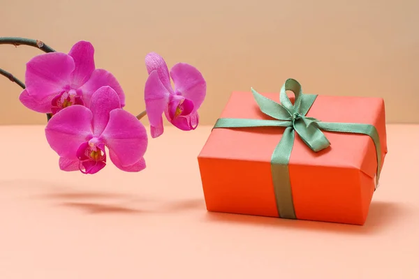 Μπουκέτο Κόκκινα Λουλούδια Ορχιδέας Και Ένα Κουτί Δώρου Στο Μπεζ — Φωτογραφία Αρχείου