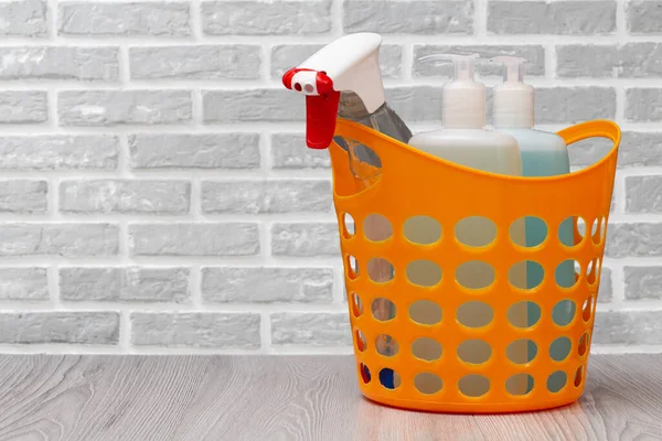 Plastic basket with bottles of dishwashing liquid, glass and tile cleaner, detergent for microwave ovens and stoves with a brick wall on the background. Washing and cleaning concept.