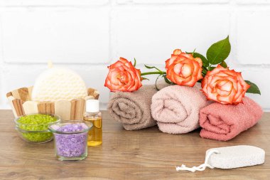 Yüz ve vücut bakımı ürünleri. Gül çiçekli yumuşak havlular, deniz tuzlu kaseler, bir şişe aroma yağı, ayak için bir sünger taşı ve ahşap zeminde sünger olan ahşap bir sepet. Spa ve vücut bakımı konsepti. Üst görünüm.
