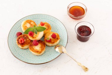 Ev yapımı kremalı börek, ahududu ve çay kaşığı. Çilek reçelli cam kaseler ve beyaz arka planda bal. Üst görünüm.
