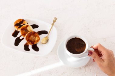 Porselen bir fincan kahveyle bir kadın eli ve çikolatayla süslenmiş ev yapımı peynirli börek tabağı. Üst görünüm.