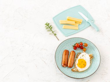 Tavada taze domatesle servis edilen kızarmış yumurta ve ızgara sosis. Kesme tahtasına dilimlenmiş peynir ve bıçak. Üst Manzara. İçten bir kahvaltı..