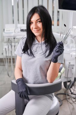 Steril eldivenli kadın dişçi diş tedavisi için aletler tutuyor. Diş aletlerini gösterirken kameraya gülümseyen kadın doktor. Diş hekimliği, stomatoloji ve diş hekimliği kavramı.