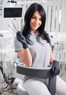 Steril eldivenli kadın dişçi diş tedavisi için aletler tutuyor. Diş aletlerini gösterirken kameraya gülümseyen sevimli bir doktor. Diş hekimliği, stomatoloji ve diş hekimliği kavramı.