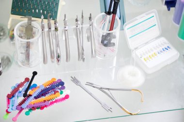 Çeşitli ortodontik enstrümanlı cam masa, parantez yerleştirme kartı ve çok renkli lastik bantlar. Diş muayenehanesinde diş teli takma prosedürü için paslanmaz çelik aletler.