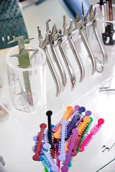 歯科事務所の机の上の様々な歯科矯正器具 歯にブレースを取り付ける手順のための多色の歯列矯正用の合字とステンレス製の楽器 歯科学の概念 — ストック写真