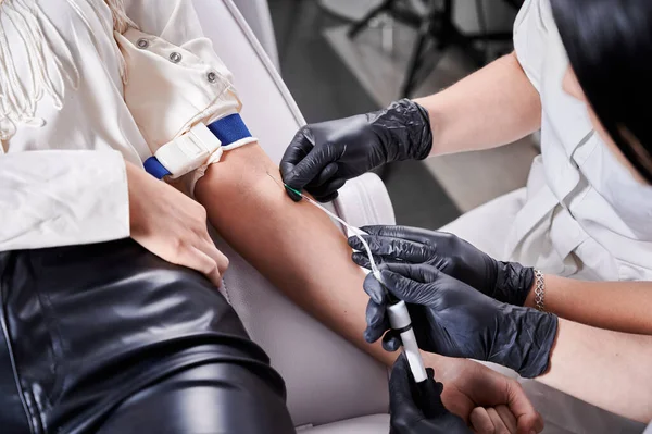 Process of taking blood sample in blood tube from a patient in a chair in beauty salon. Young brunette girl sitting in chair before platelet-rich plasma therapy. Concept of modern beauty treatment
