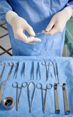 Doktor elleri plastik cerrahi için paslanmaz çelik neşter hazırlıyor. Masada çeşitli alet ve gereçler var. Beyaz steril eldivenli bir cerrah. Tıp kavramı.