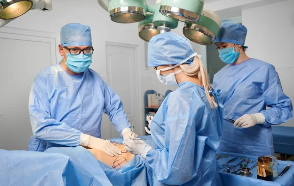 手術室で美容整形を行う青い外科用制服の医師のグループ 外科チームは審美的な手術を行い 診療所で医療機器を使用しています 整形手術の概念 — ストック写真