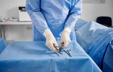 Steril eldivenli plastik cerrah tıbbi aletleri kontrol ediyor. Doktor ameliyat için makas, pens ve neşter hazırlıyor. Estetik ameliyat hazırlığı kavramı.
