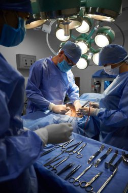 Cerrahi ekip ameliyathanede estetik ameliyat yapıyor. Doktorlar estetik ameliyat yaparken asistan tıbbi aletlerle ameliyat masasında duruyor. Tıp ve estetik cerrahi kavramı.