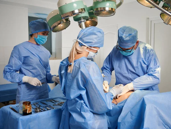 手術室で美容整形を行う医師のグループ 診療所で審美的な手術を行いながら 保護面マスク 滅菌手袋 医療キャップを身に着けている外科チーム — ストック写真