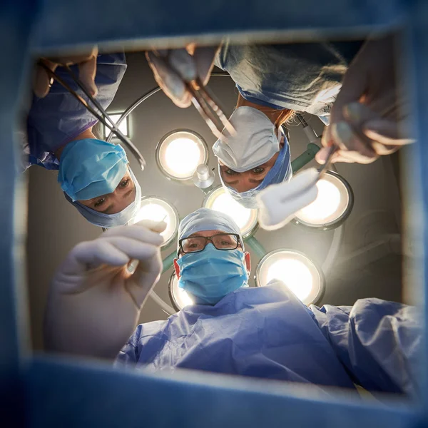手術中の患者を見ながら医療機器を保持している医療チームの下からの眺め手術室で手術をしている間 フェイスマスクと滅菌手袋を着用してください 薬の概念 — ストック写真