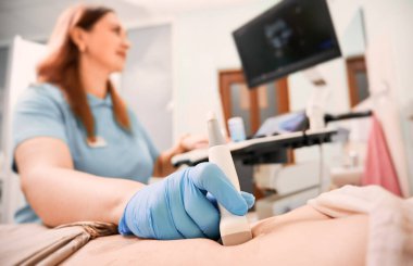 Focus on sonographer's hand in sterile glove examining woman with ultrasound scanner. Female doctor moving transducer on patient abdomen while looking at display. Concept of ultrasound diagnostics. clipart