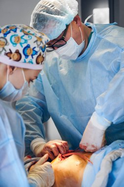 Ameliyat kıyafetleri içinde tıbbi işçiler ameliyathanede karın gerdirme ameliyatı yapıyorlar. Yüz maskesi ve steril eldiven takan plastik cerrah ve asistan hasta karnındaki fazlalıkları temizlerken....