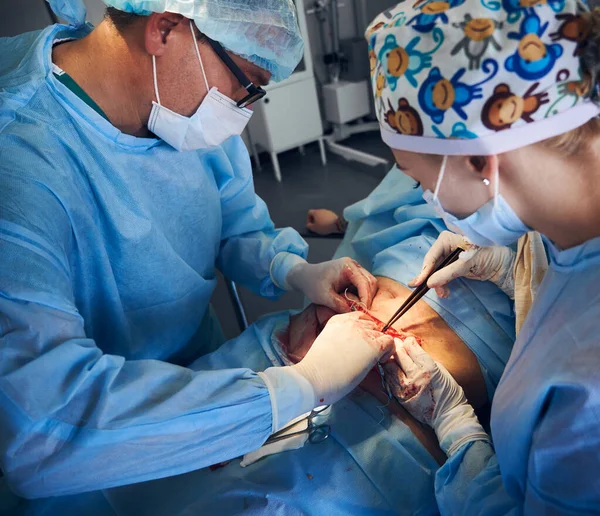 Medical workers performing plastic surgery in operating room. Male doctor and female assistant removing excess fat from patient abdomen. Concept of medicine, abdominoplasty and cosmetic surgery.